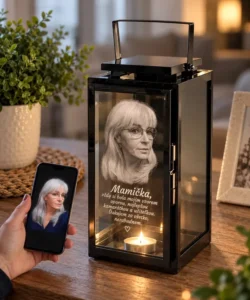 Sklenený kahanec s fotografiou zosnulého | Gravírovanie fotiek do skla - darček s venovaním Memorial lantern with a photo of an elderly woman and a lit candle inside; a hand holds a phone displaying the same image beside it.