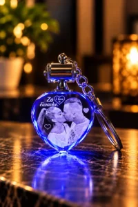 Blue, heart-shaped keychain with a glowing base and a photo of a couple kissing etched on it; metal top and chain.